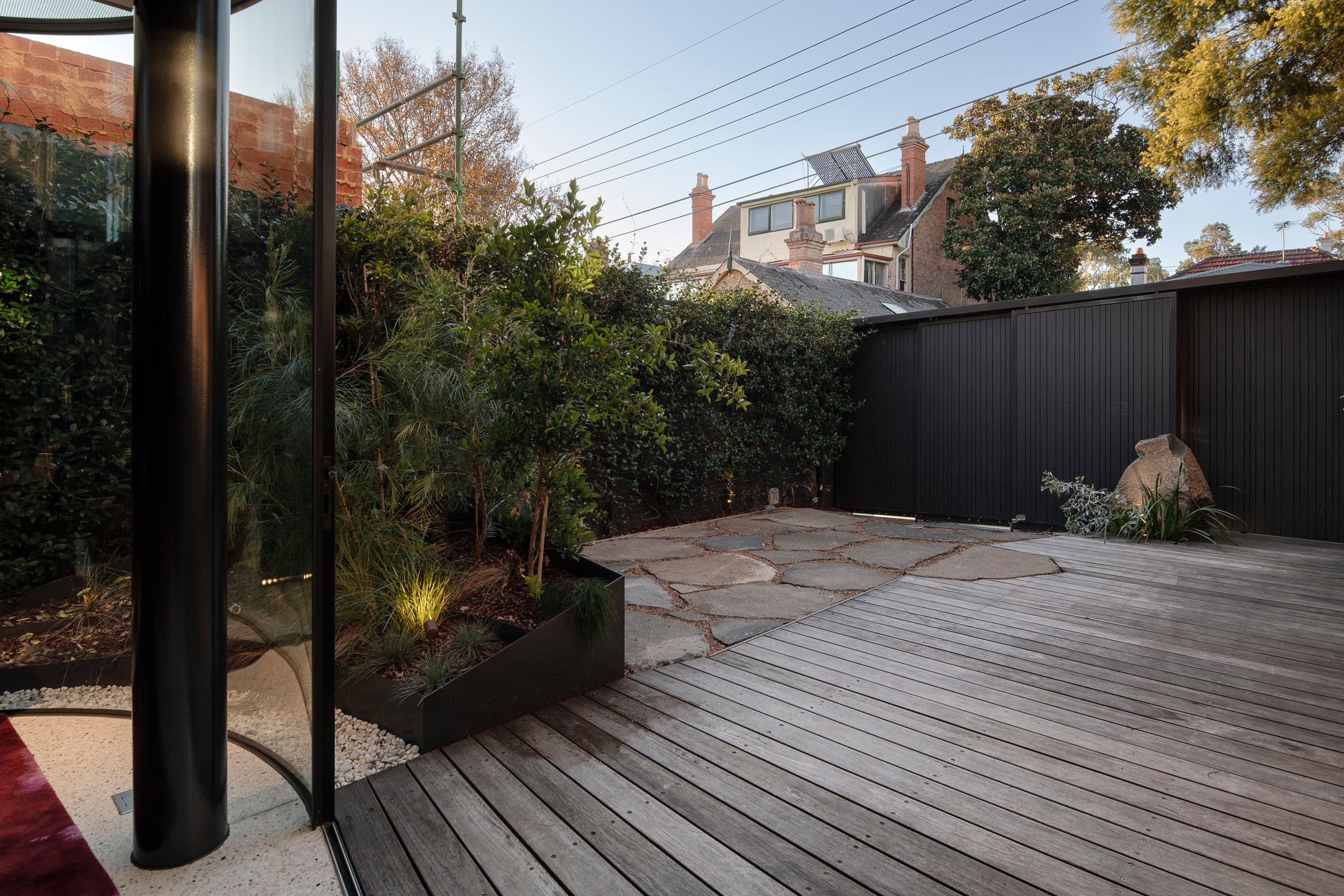 Landscaped courtyard with a timber deck, irregular stone paving and a black clad screen wall