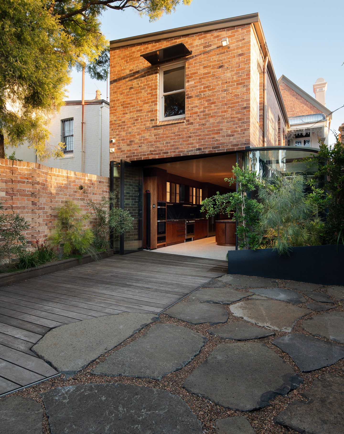 Restored brick home with a glass-walled kitchen opening onto a timber deck and stone courtyard